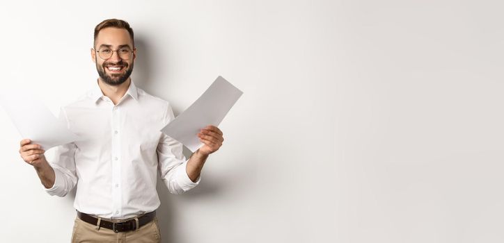 Satisfied boss smiling while holding good report, reading documents, standing over white background
