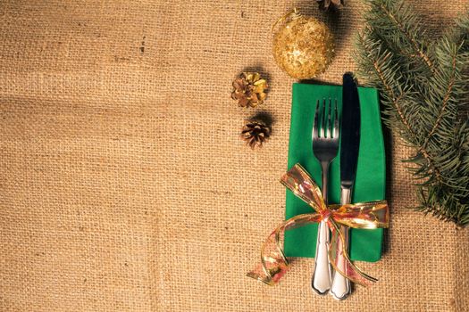 Knife and fork on green napkin and natural fir tree branch on sackcloth