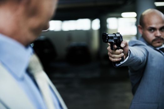 Dont make me put a bullet in your skull. A criminal aiming his handgun at a surprised executive in a dark parkade.