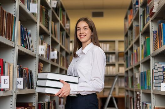 Young female student puts books on a shelf in a public library.