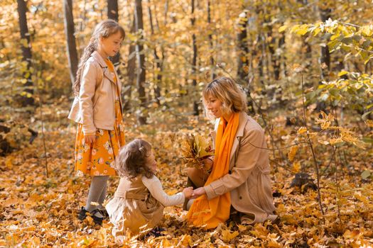 Young mother with her little daughters in an autumn park. Fall season, parenting and children concept.