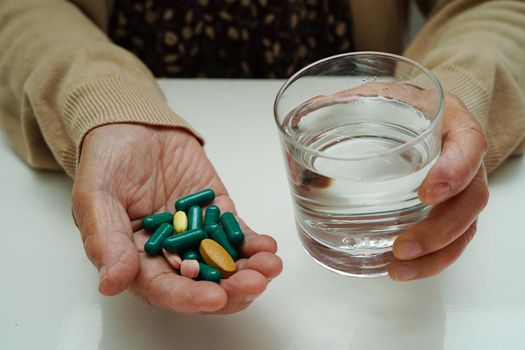 Asian elderly woman holding pill drug with water in glass, strong healthy medical concept.