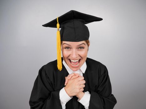 Caucasian woman in graduate gown dreamily holds her hands on her chest.