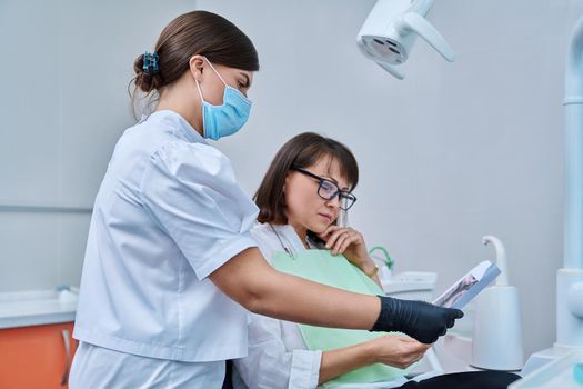 Female dentist talking to woman patient, discussing x-rays of teeth and jaws