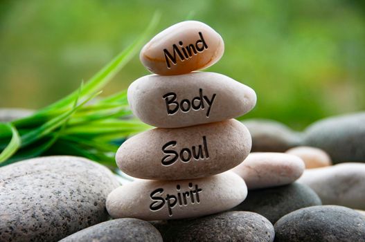 Mind, Body, Soul and Spirit words engraved on zen stones with blurred nature background. Copy space and zen concept