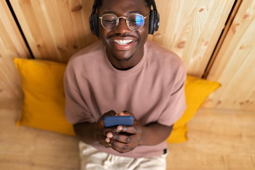 High angle view of young black man Listening to music with wireless headphones using mobile phone at home.