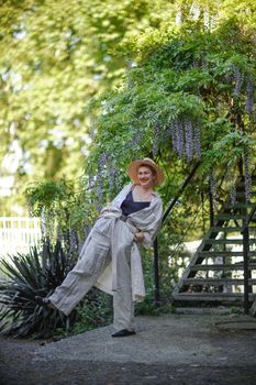 Thoughtful happy mature woman in hat surrounded by chinese wisteria