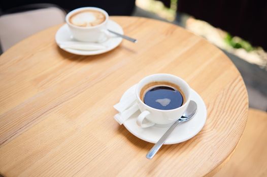 Top view of white cups of aromatic coffee americano and cappuccino on a wooden table, in the summer terrace of a cafeteria. Food and drink. Copy advertising space. Still life