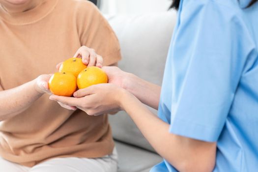 A young caregiver handing oranges to her contented senior patient at home.