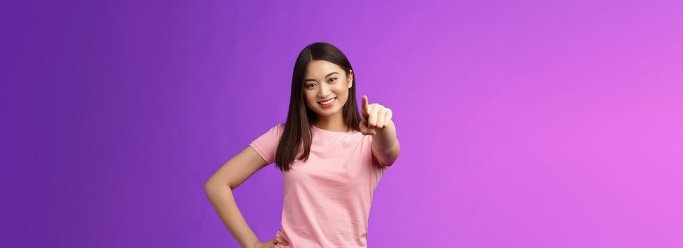 We need you our team. Friendly good-looking outgoing asian woman brunette pointing camera, indicate index finger, smiling motivated, picking person, making decision, stand purple background