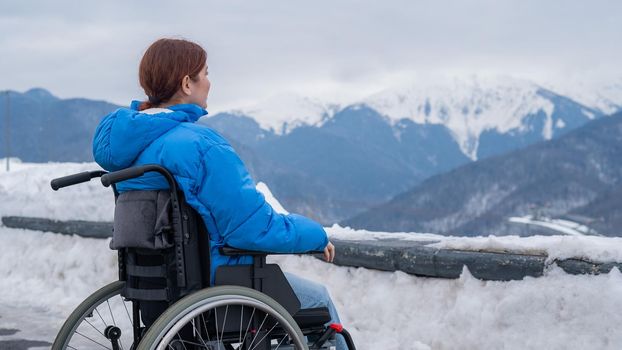 Rear view of a woman in a wheelchair travels in the mountains in winter.