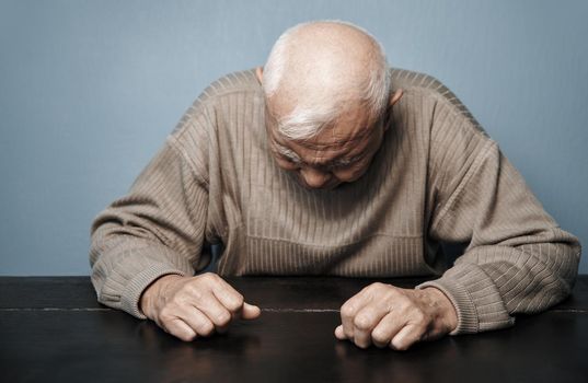 Senior man feeling headache and negative emotions while sitting at the table