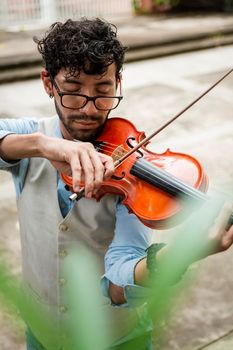 Handsome man in vest playing violin outdoors. Close up of violinist man playing a melody outdoors. Violinist artist playing a melody outdoors.