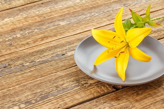 Plate with lily flower on the wooden background.