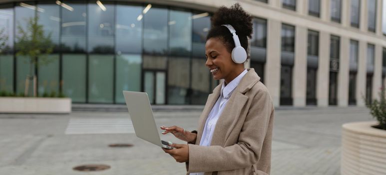 young African American woman cybersecurity specialist with a laptop in her hands and headphones on the background of the office center