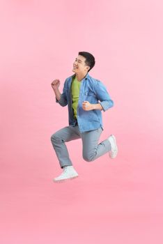 Energetic happy young Asian man jumping isolated in pink background