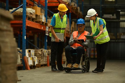 Male manager in wheelchair and workers working together in warehouse. Manufacture storehouse occupation concept