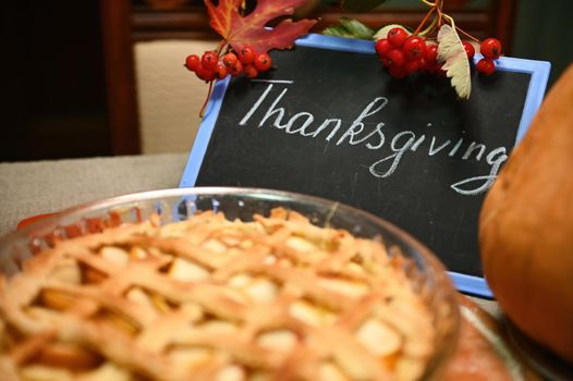 A chalk board with lettering Thanksgiving Day and sweet homemade classic American pumpkin apple pie with crispy crust