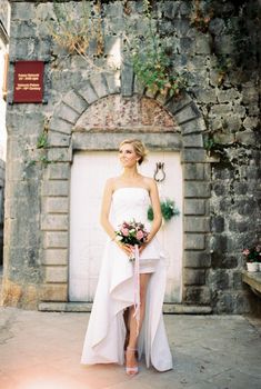 Bride in a white dress with a cutout stands near an ancient stone building