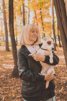 Senior smiling woman hugging her dog in autumn park. Active aging and pet concept.