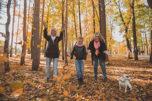 Grandmother and mother with granddaughter throw up fall leaves in autumn park and having fun. Generation, leisure and family concept.