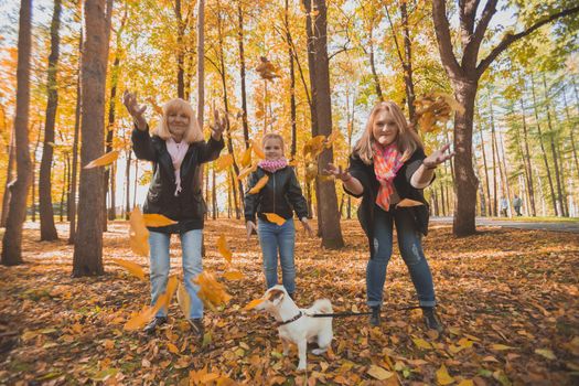 Grandmother and mother with granddaughter throw up fall leaves in autumn park and having fun. Generation, leisure and family concept.