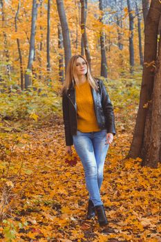 Girl holds fallen leaves and walks in autumn park. Seasonal concept.
