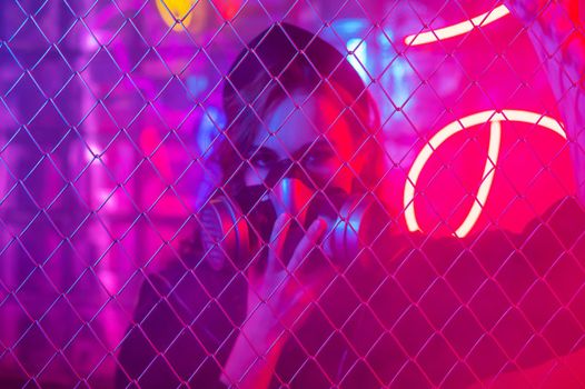Caucasian woman in a gas mask behind a fence in a neon studio.