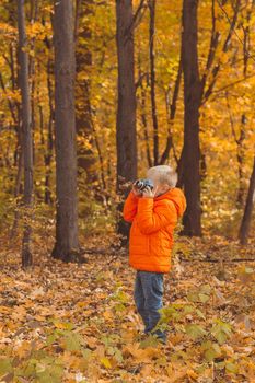 Boy with retro camera taking pictures outdoor in autumn nature. Leisure and photographers concept