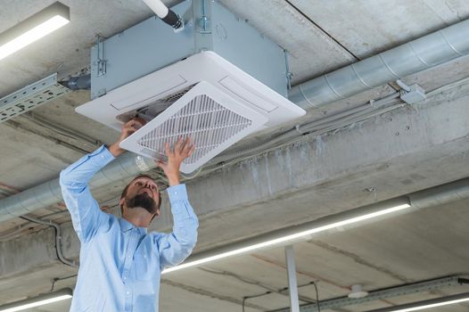 Caucasian bearded man repairing the air conditioner in the office.
