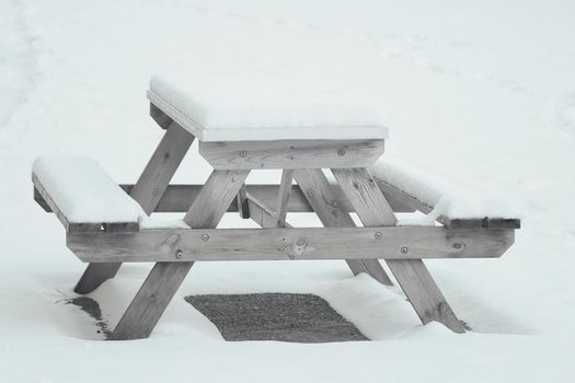 An empty bench in the park is covered with snow.