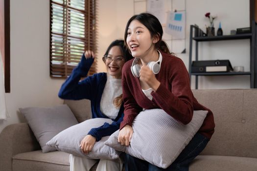 Two Young woman cheering together for sport on TV in cozy living room at home