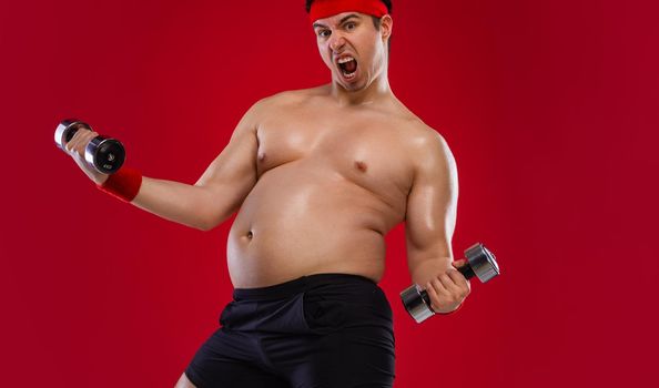 Fat man doing workout traning with dumbbells. Athlete isolated over red background.