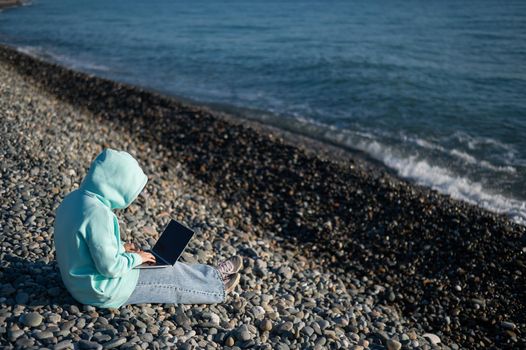 Caucasian woman working freelance on laptop on the beach.