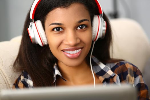 Smiling woman with headphones on sofa and listening to music