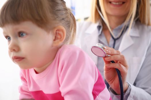 Pediatrician listens to lungs of small child girl with stethoscope