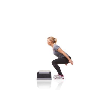 Crouched and ready to meet her fitness goals. A smiling young woman doing aerobics on an aerobic step against a white background.