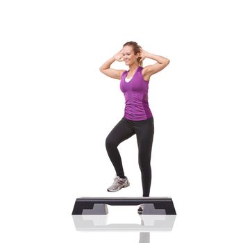 Stepping up her fitness regime. A smiling young woman doing aerobics on an aerobic step against a white background.