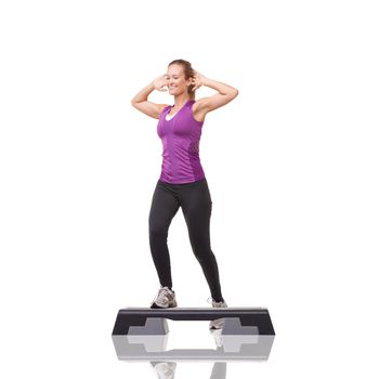 Taking steps to improve her fitness. A smiling young woman doing aerobics on an aerobic step against a white background.