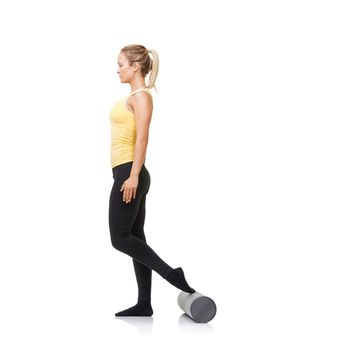 Stretching out her leg muscles. A young woman standing and using a foam roller while isolated on white.