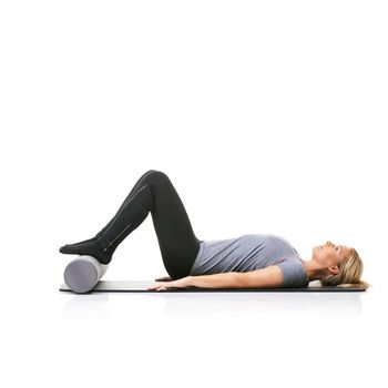 Getting ready to do some crunches. A young woman lying on an exercise mat with her feet on a foam roller.