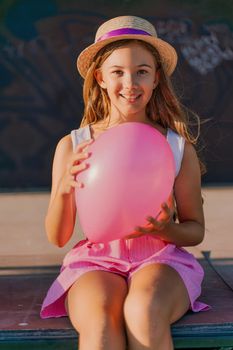Portrait of a girl in a hat with a pink balloon. She is dressed in pink clothes and her hair is long and loose.