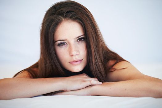 Get lost in her gaze. A natural young beauty with brunette hair looking at you while lying in bed.