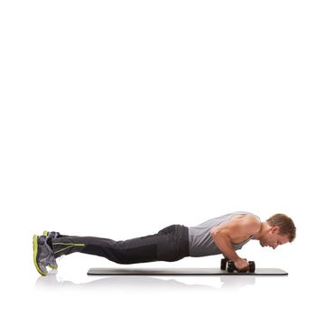 Exertion and exercise. A fit young man doing push-ups with a pair of dumbbells.