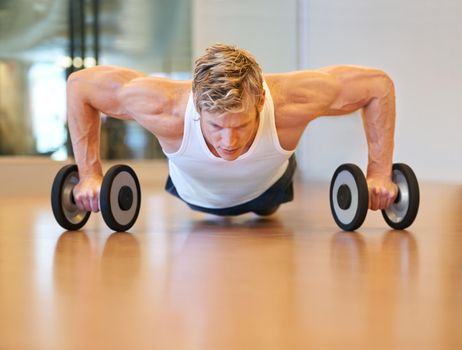 Hes in excellent shape. Fit young man doing push ups in a health club using dumbbells.