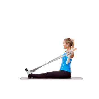 Building those biceps. A young blonde woman sitting on a mat and exercising with a resistance band - profile.