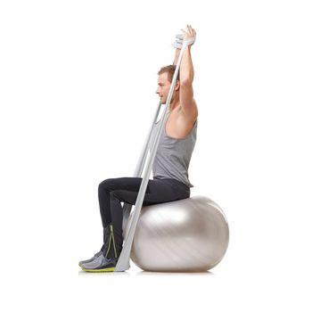 Using the tools of the toning trade. Young man sitting on a Swiss ball and pulling a resistance band.