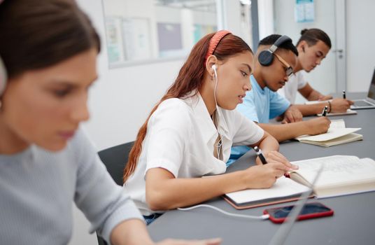 University, headphones and students writing notes while listening to music, educational podcast or radio audio. Earphones, college and group learning, studying or exam preparation with phone on desk.