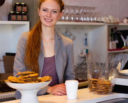 Here for your satisfaction. Smiling young baker standing happily behind her serving counter - portrait.
