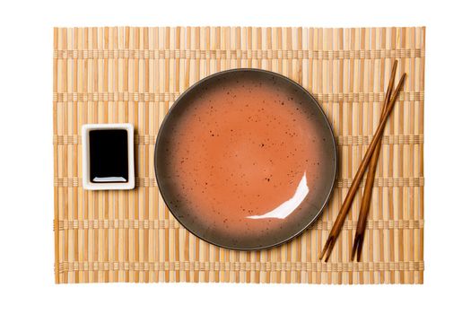 Empty round brown plate with chopsticks for sushi and soy sauce on yellow bamboo mat background. Top view with copy space for you design